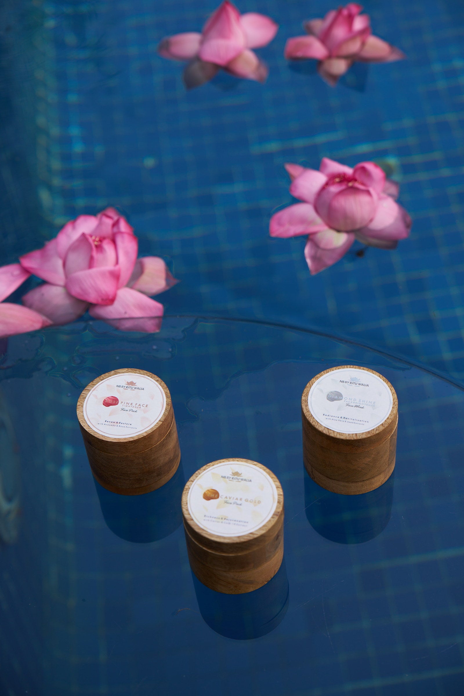 The three NB face packs arranged on glass above still water with lotus blooms
