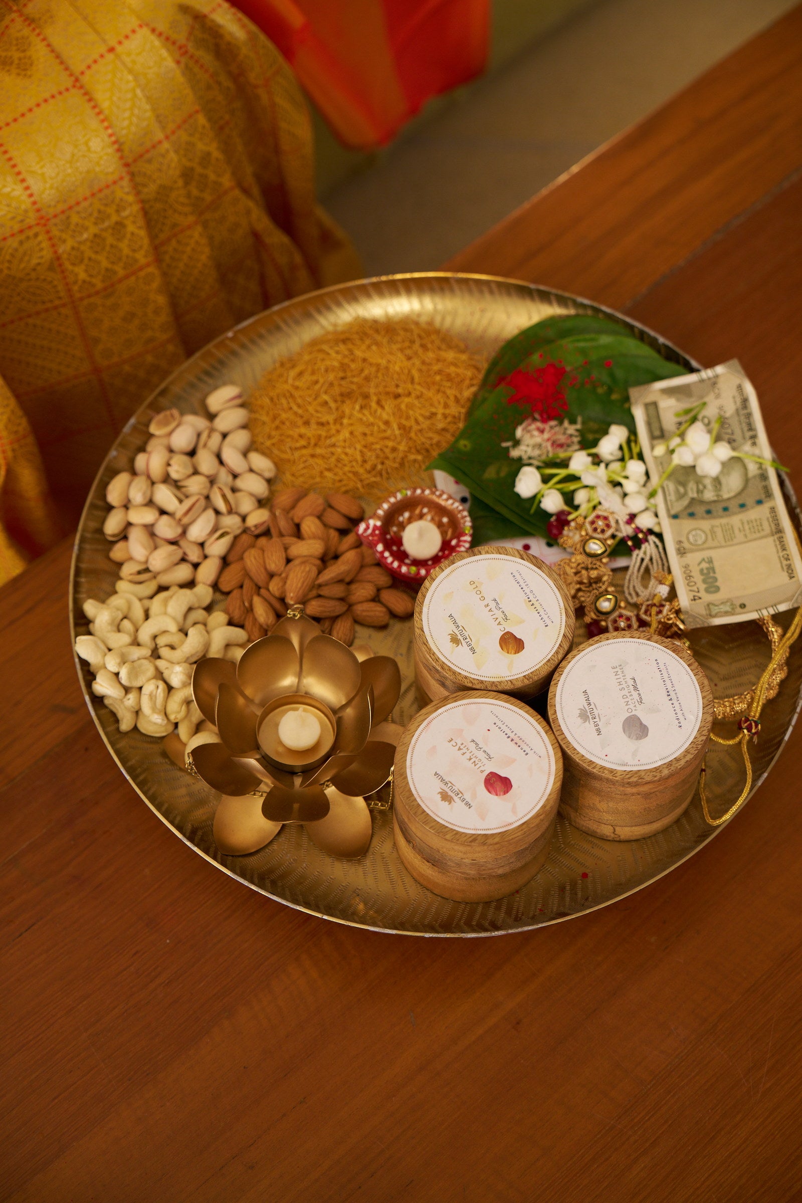 The three NB face packs set into a brass festive thali with dry fruits, a diya and rakhi threads